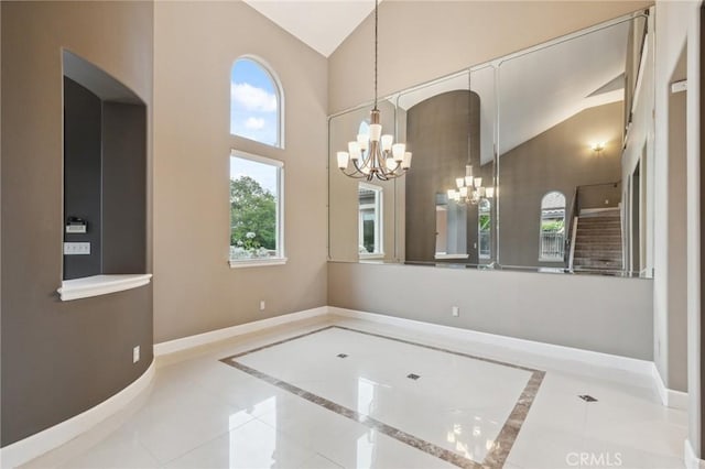 unfurnished dining area featuring an inviting chandelier, tile patterned floors, high vaulted ceiling, and baseboards