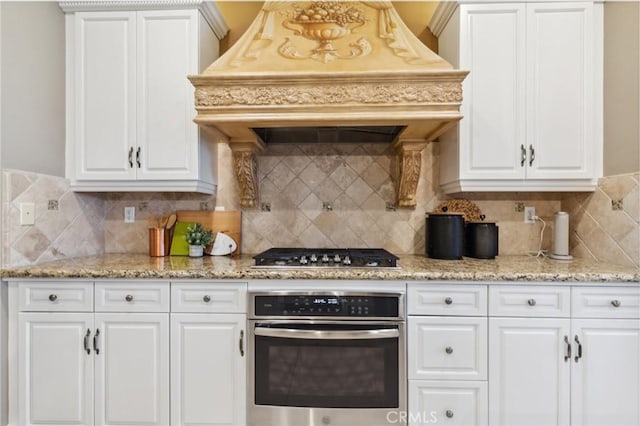 kitchen with custom exhaust hood, white cabinets, appliances with stainless steel finishes, and decorative backsplash