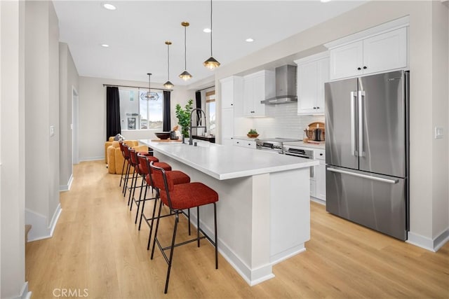 kitchen featuring baseboards, white cabinets, appliances with stainless steel finishes, and wall chimney range hood