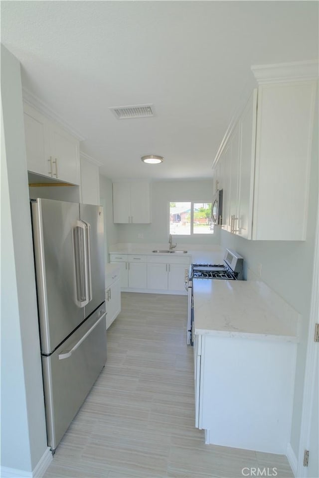 kitchen featuring a sink, stainless steel appliances, visible vents, light stone counters, and white cabinetry
