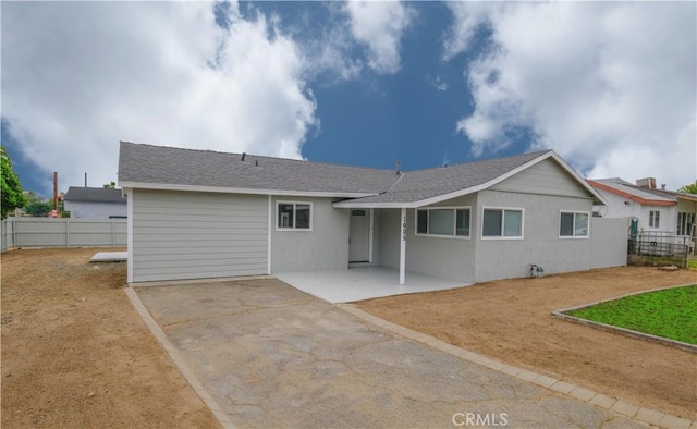 rear view of house featuring fence, a shingled roof, driveway, and a patio area