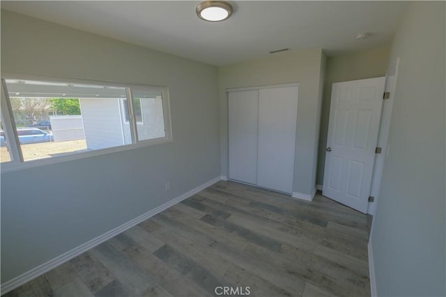 unfurnished bedroom featuring baseboards, visible vents, wood finished floors, and a closet