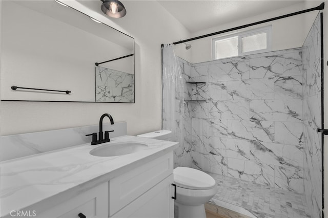 bathroom with toilet, a marble finish shower, and vanity