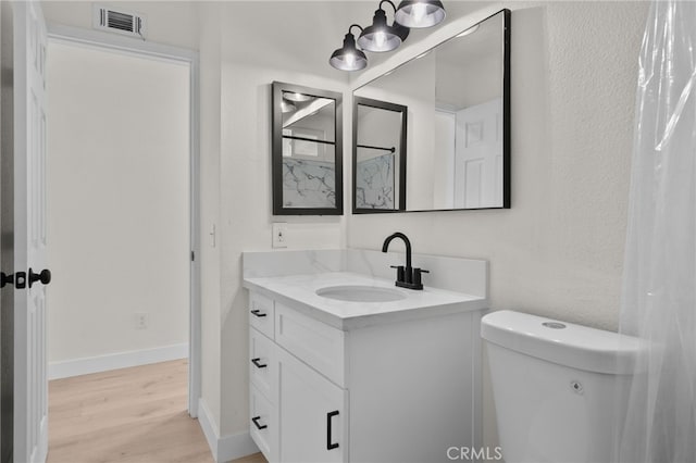 bathroom with vanity, toilet, visible vents, baseboards, and wood finished floors