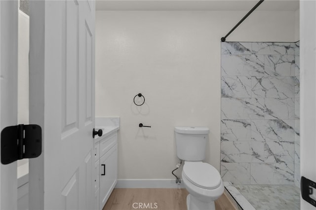 bathroom with tiled shower, toilet, wood finished floors, and vanity