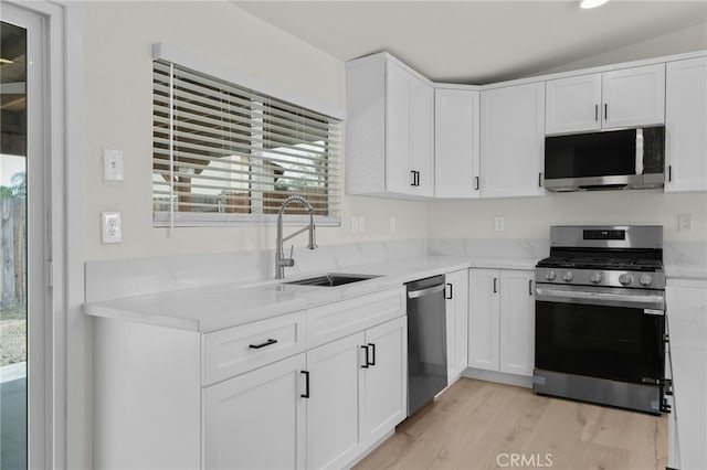 kitchen featuring light stone countertops, a sink, light wood-type flooring, white cabinets, and appliances with stainless steel finishes