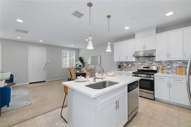 kitchen featuring under cabinet range hood, appliances with stainless steel finishes, a sink, visible vents, and open floor plan
