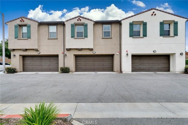 view of property featuring stucco siding, a tiled roof, and a garage