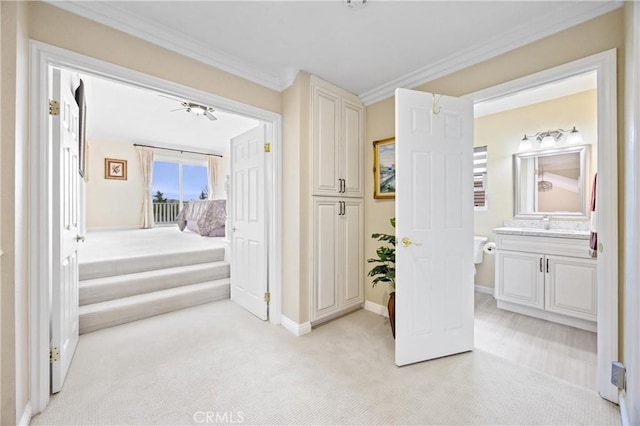 hallway featuring crown molding, baseboards, light colored carpet, and a sink