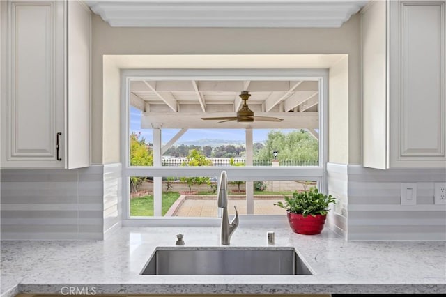 room details featuring ceiling fan, tasteful backsplash, a sink, light stone counters, and white cabinetry