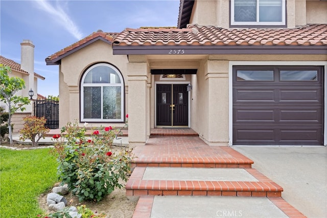 view of exterior entry with a garage, stucco siding, and a tile roof