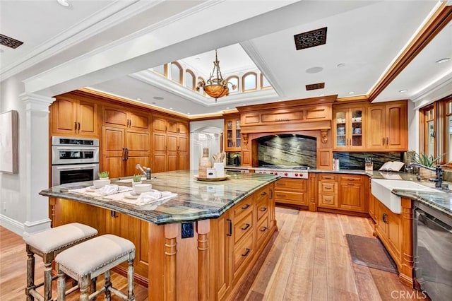 kitchen with brown cabinets, appliances with stainless steel finishes, a sink, light wood-style floors, and glass insert cabinets