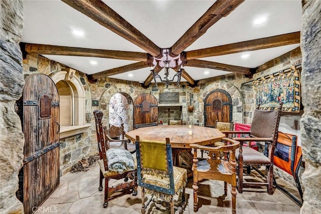 dining area featuring arched walkways, beamed ceiling, a ceiling fan, and stone finish flooring