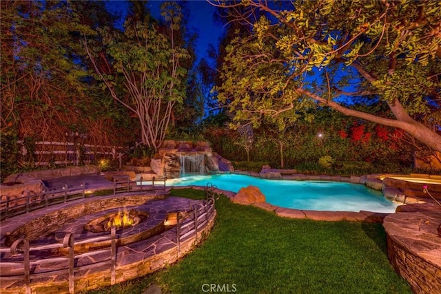 pool with a lawn, fence, a hot tub, and an outdoor fire pit