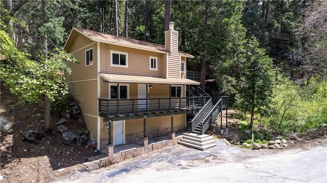 26131 Lake Forest Dr, Twin Peaks, CA 92391 - view of front of house featuring a chimney, roof with shingles, stairway, stone siding, and a wooded view