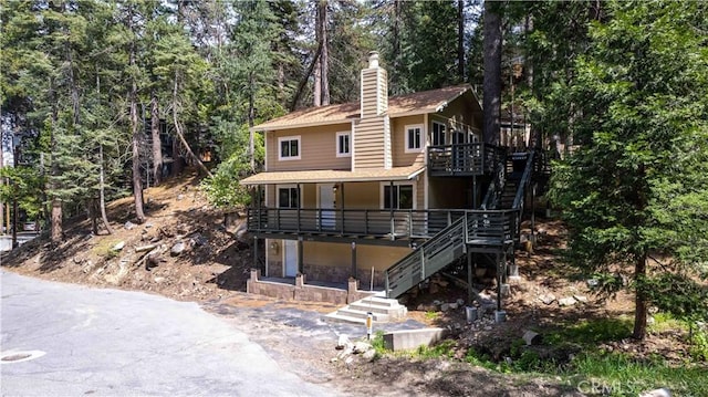 26131 Lake Forest Dr, Twin Peaks, CA 92391 - view of front facade with stairway, a chimney, a wooden deck, roof with shingles, and view of scattered trees