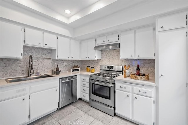kitchen with decorative backsplash, a sink, under cabinet range hood, stainless steel appliances, and white cabinetry