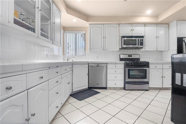 kitchen with appliances with stainless steel finishes, white cabinetry, decorative backsplash, and tile countertops