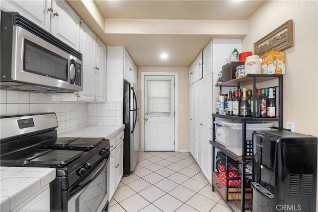 kitchen featuring light tile patterned floors, stainless steel appliances, white cabinets, and tile countertops