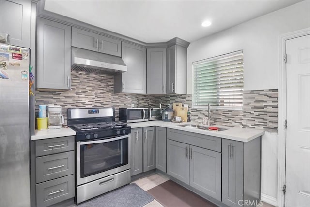 kitchen featuring gray cabinets, stainless steel appliances, under cabinet range hood, light countertops, and a sink