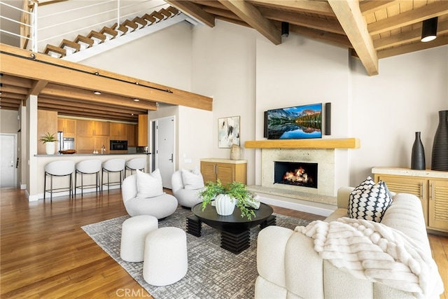 living room featuring beamed ceiling, a premium fireplace, and wood finished floors