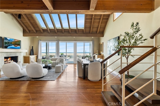 living room featuring wood finished floors, stairs, beamed ceiling, high vaulted ceiling, and a lit fireplace