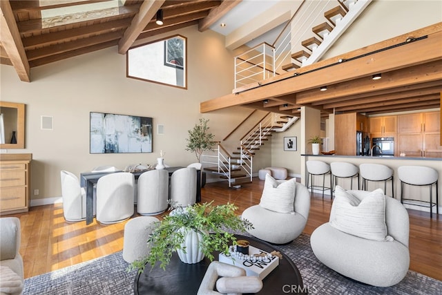 living area featuring beamed ceiling, stairway, wood-type flooring, high vaulted ceiling, and baseboards