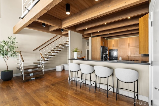 kitchen with beamed ceiling, a kitchen bar, black appliances, baseboards, and dark countertops