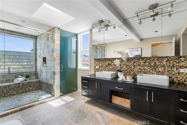full bathroom featuring a sink, a stall shower, double vanity, backsplash, and a skylight