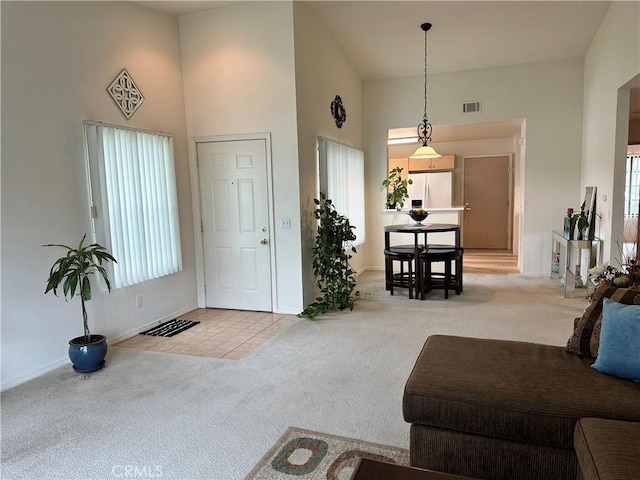 carpeted living area with baseboards, a high ceiling, tile patterned flooring, and visible vents