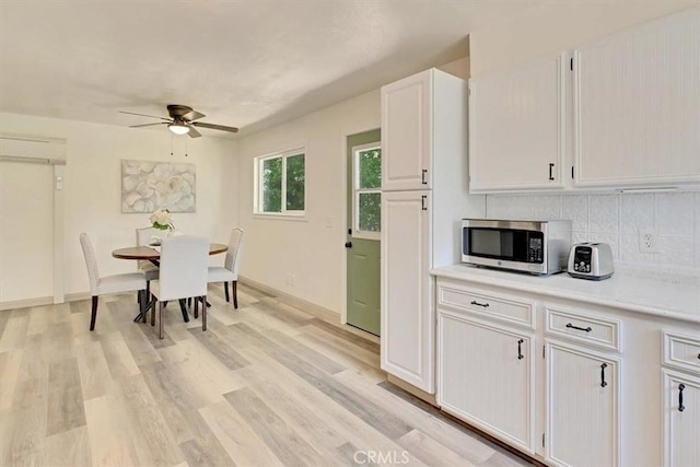 kitchen with stainless steel microwave, ceiling fan, backsplash, light countertops, and white cabinets