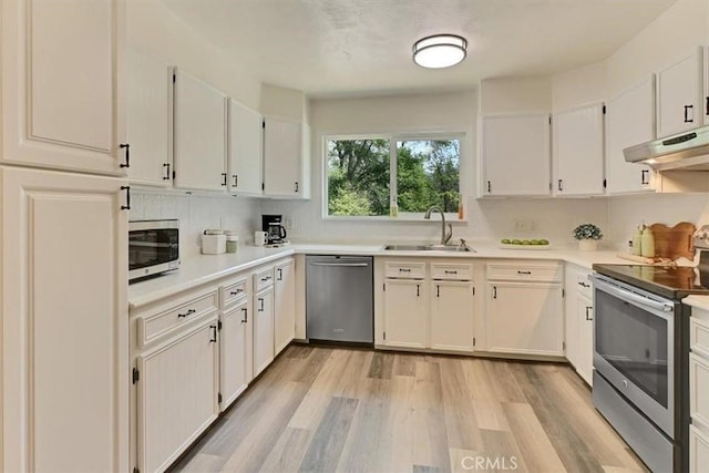 kitchen with a sink, stainless steel appliances, under cabinet range hood, light wood-style flooring, and light countertops