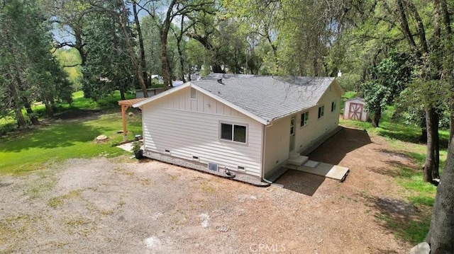 rear view of house featuring an outdoor structure, board and batten siding, a storage shed, roof with shingles, and crawl space
