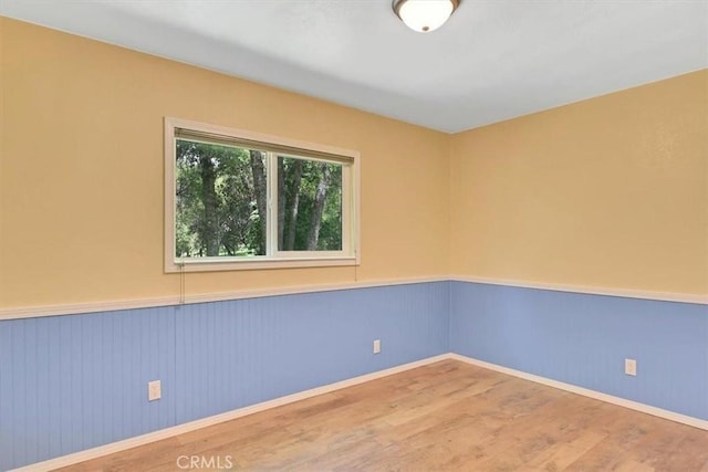 spare room with baseboards, wood finished floors, and a wainscoted wall