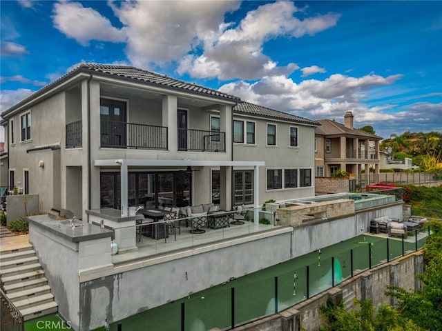 back of house with a tile roof, a balcony, a patio, outdoor lounge area, and stucco siding