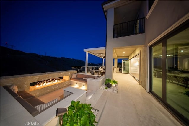 patio at twilight featuring an outdoor fire pit and a balcony