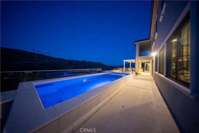 pool at night featuring a patio, an outdoor pool, and an in ground hot tub