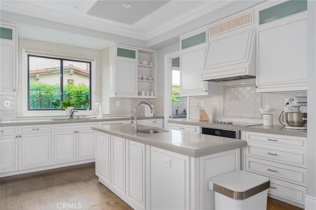 kitchen with light countertops, ornamental molding, a sink, and a kitchen island with sink