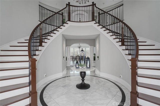 foyer entrance featuring baseboards, stairs, a high ceiling, and a chandelier