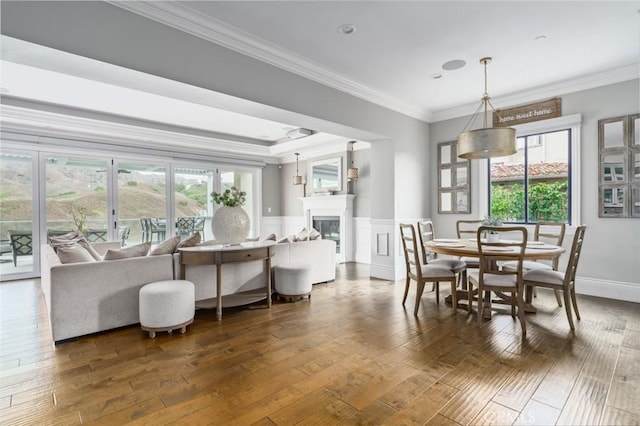 dining area with wainscoting, dark wood finished floors, ornamental molding, and a glass covered fireplace