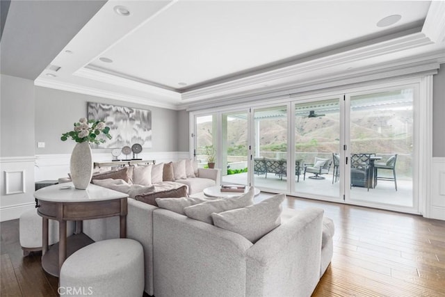 living area featuring crown molding, a wainscoted wall, wood-type flooring, and a tray ceiling