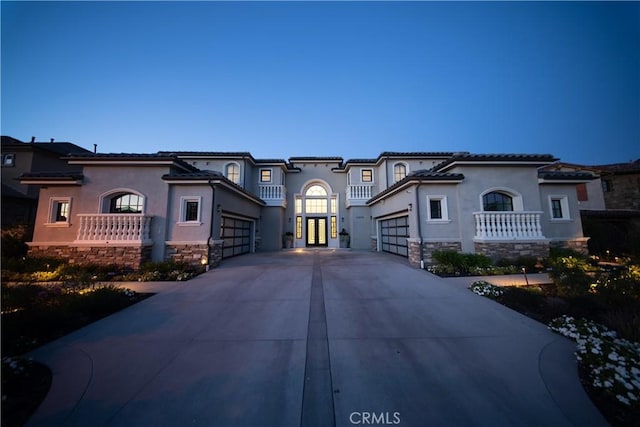 mediterranean / spanish house featuring an attached garage, driveway, stone siding, and stucco siding