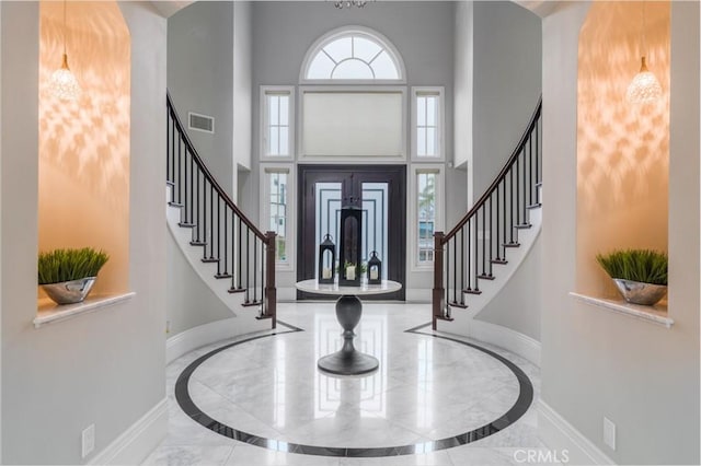 foyer entrance with baseboards, stairs, a high ceiling, and visible vents