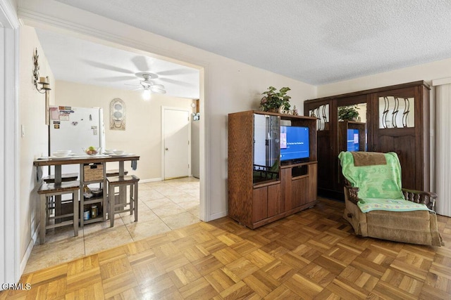 living area featuring baseboards, a textured ceiling, and ceiling fan