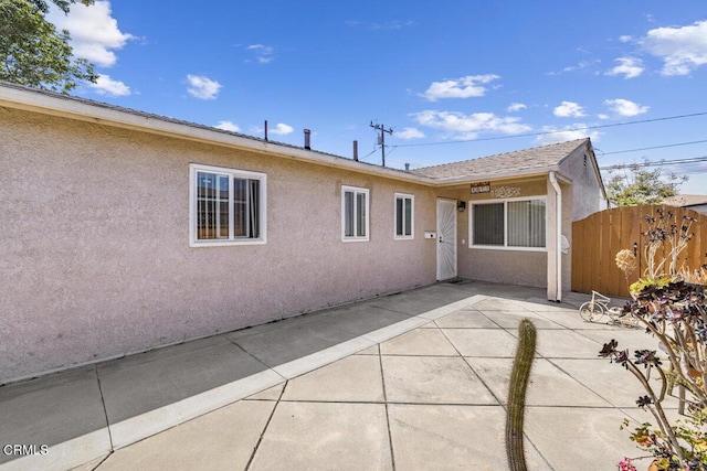 rear view of house with fence, a patio area, and stucco siding