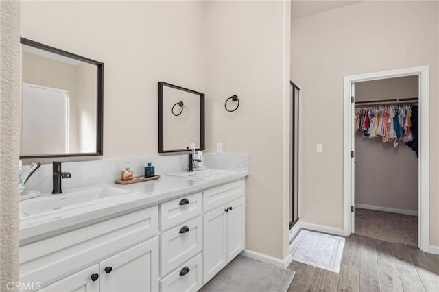 full bathroom featuring a stall shower, double vanity, a sink, and wood finished floors