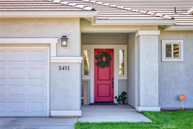 entrance to property with a garage, stucco siding, and a tiled roof