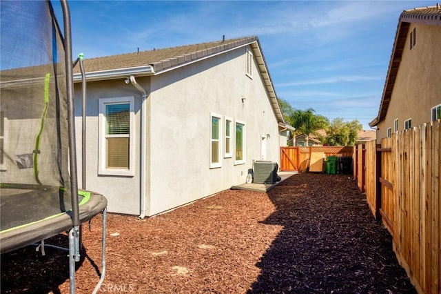 rear view of house with a trampoline, a fenced backyard, and stucco siding