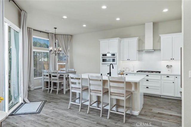 kitchen featuring light wood-type flooring, an island with sink, wall chimney exhaust hood, and gas stovetop