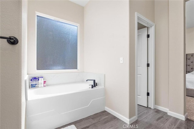 ensuite bathroom featuring connected bathroom, a bath, wood finished floors, and baseboards